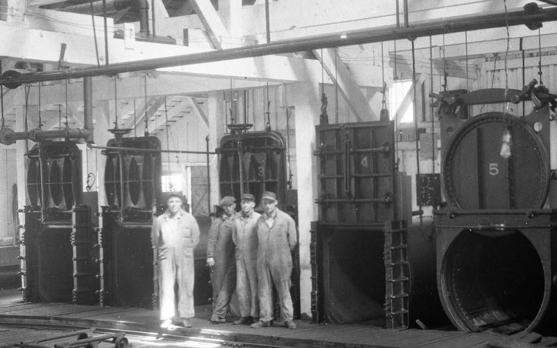 Quatre hommes se tiennent debout devant cinq autoclaves de cuisson vides et ouverts.