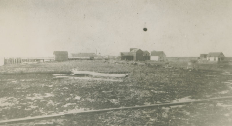 Bâtiments dispersés à travers une étendue de terre plate et en majeur partie stérile.