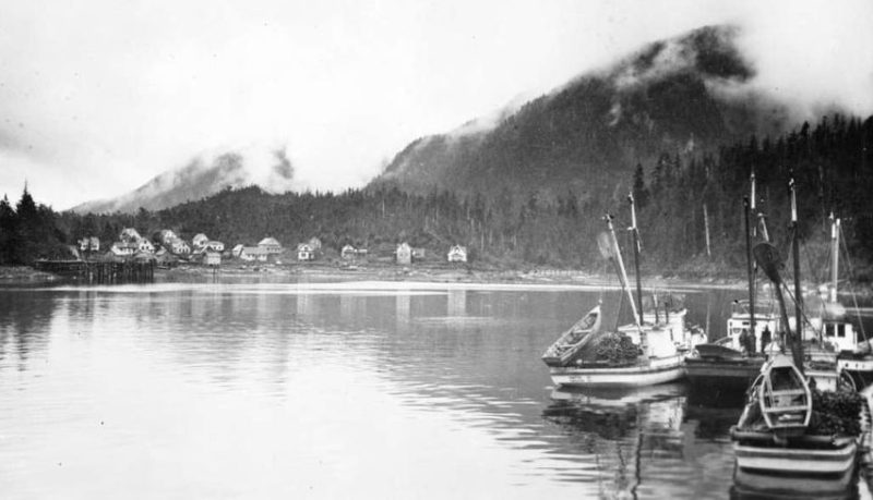 Klemtu Cannery buildings on the distant shore with fishing boats in the foreground.