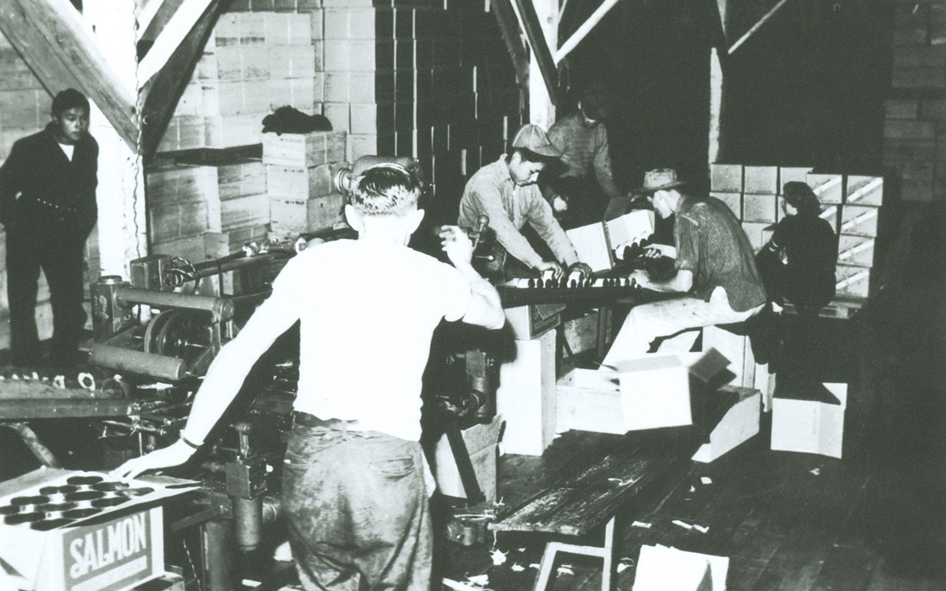 Six workers and labeling machine at the North Pacific Cannery. One box in the foreground bears the label "Salmon."