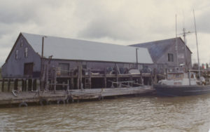 Les bâtiments du camp de pêche de la conserverie Pacific Coast et des bateaux amarrés au quai en avant-plan.