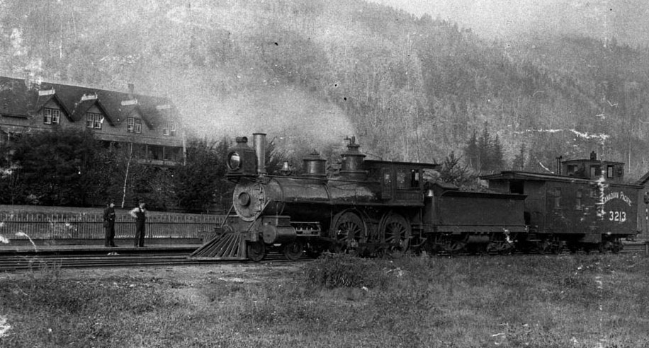 Two men stand looking at a Canadian Pacific train engine on a track. The train car reads "Canadian Pacific 3213."