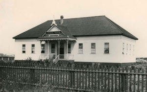 Bâtiment blanc d'un seul étage avec une petite galerie derrière une clôture
