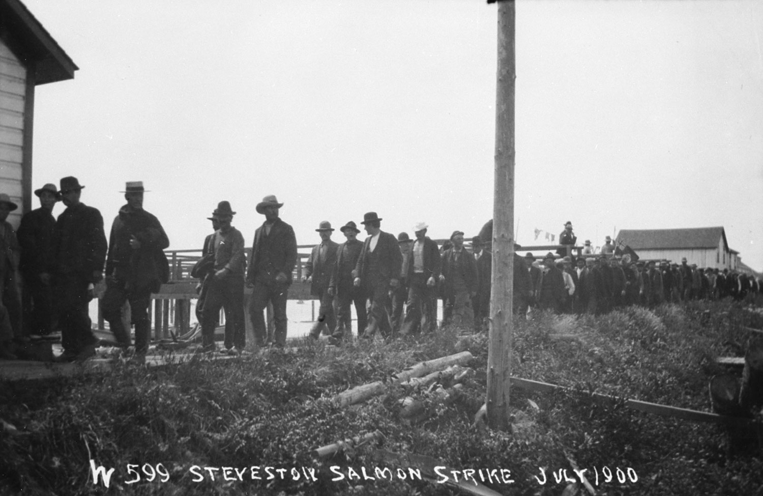 Men walk in a long line on a path on the dike along the Steveston waterfront.