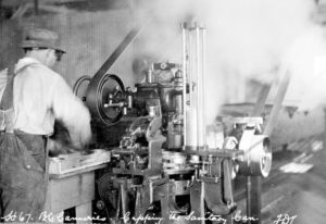 A worker operates a machine putting lids on cans. There is steam above the machine.
