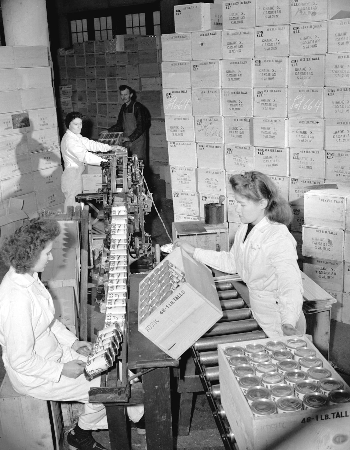 Workers labeling and crating one pound cans. Crates are stacked to the ceiling in the background.