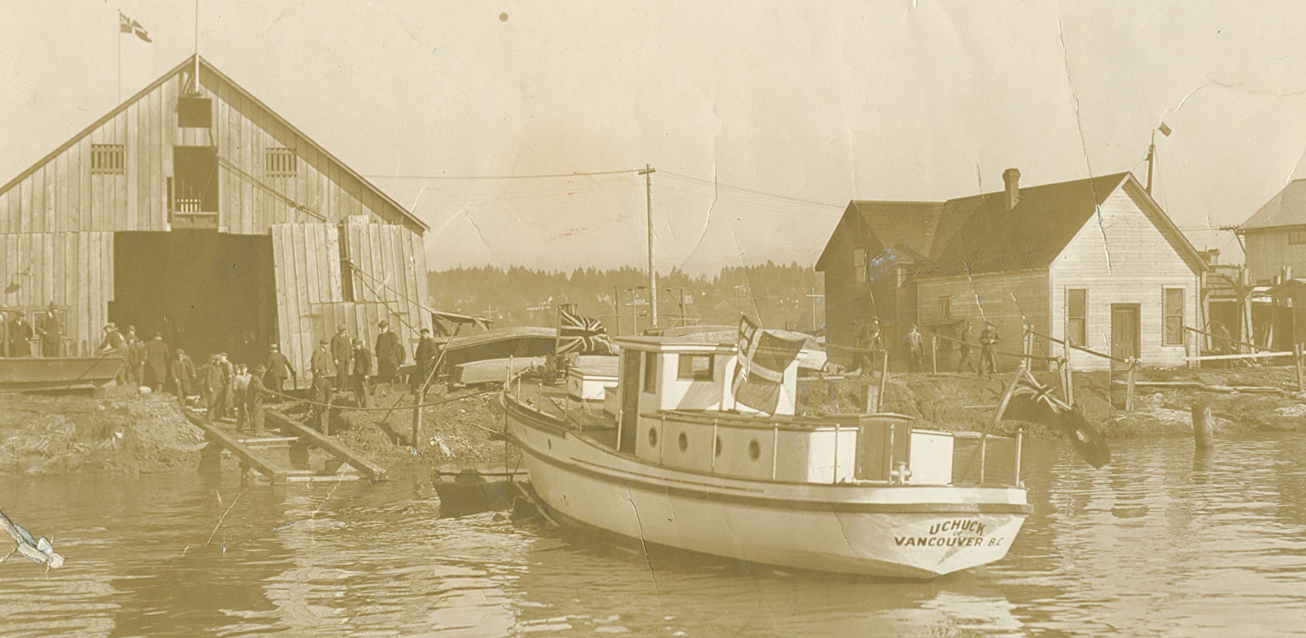 Workers standing in front of a wooden boat shed preparing to bring a boat into a dry dock.
