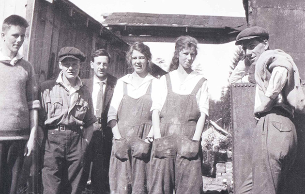 Groupe d'ouvriers de conserverie se tenant debout à l'extérieur. Deux travailleuses portent des couvre-tout et ont les mains dans les poches.