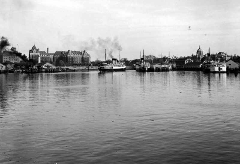 Vue du port intérieur de Victoria prise de l'eau et montrant l'hôtel Empress et les bateaux à vapeur.