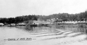 Cannery buildings in the distance across the water. "Cannery at Bella Bella" written at the bottom of the image.