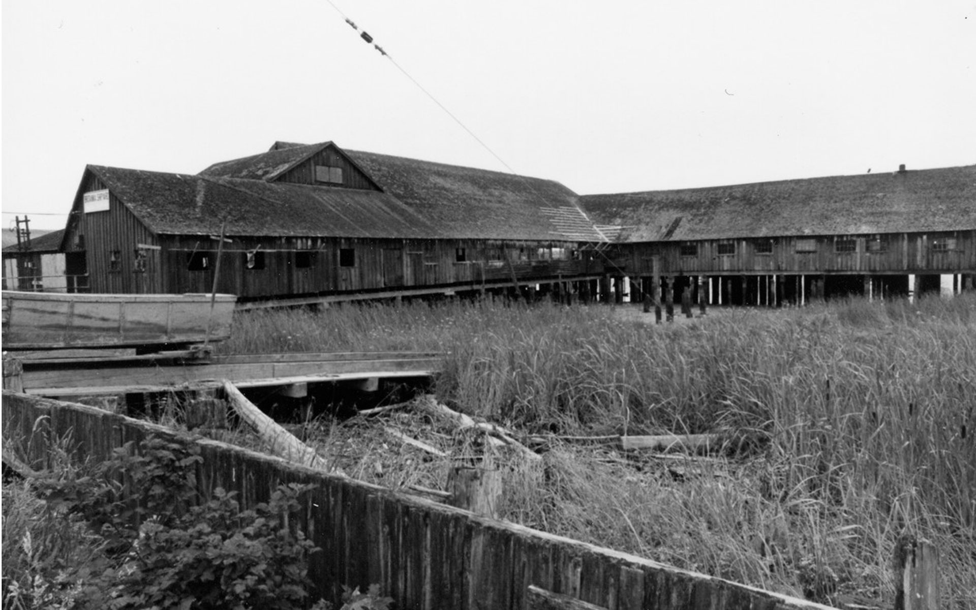 Britannia Shipyards buildings at low tide with grasses in the foreground.