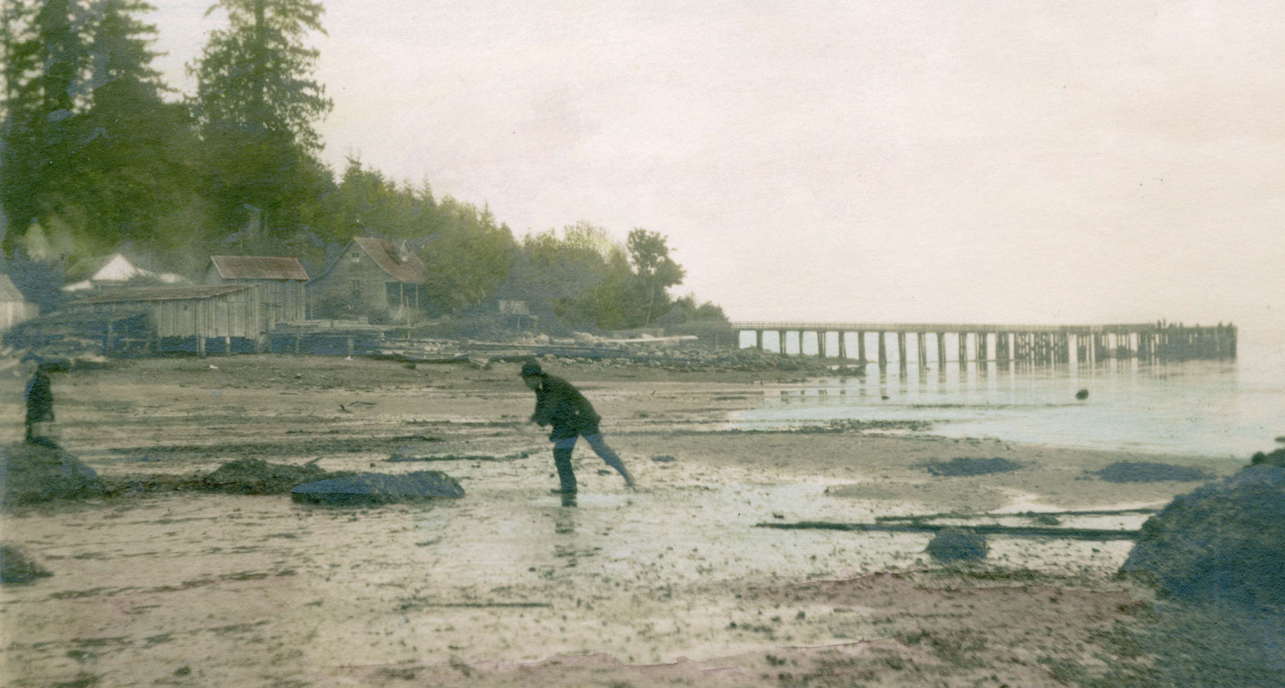 Two figures on the beach at low tide in front of the English Bay Cannery.