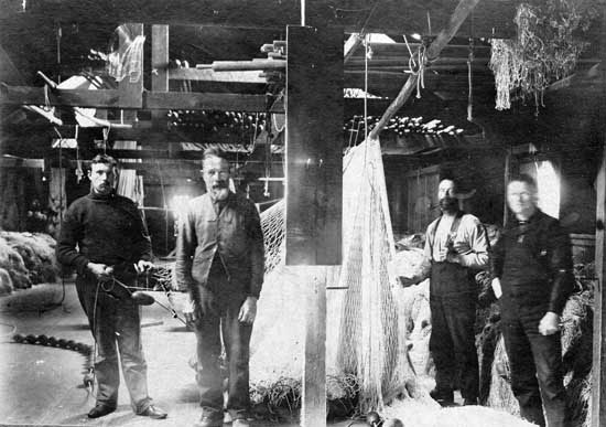 Four men stand surrounded by nets in the interior of a cannery.