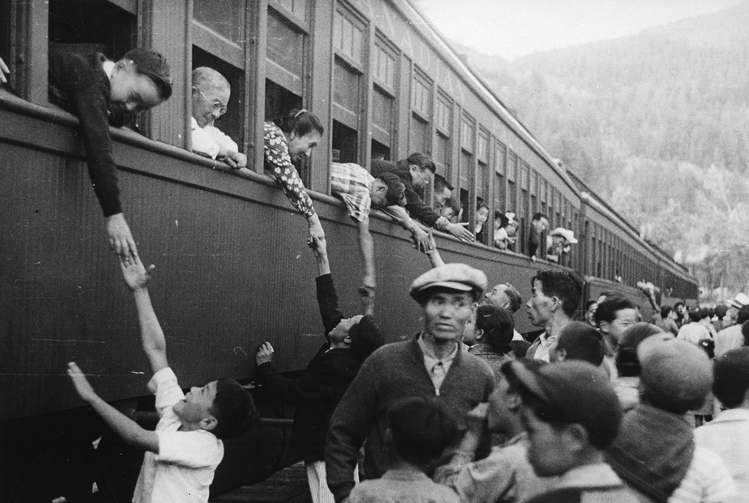 Japanese evacuees lean out of train windows to hold hands with people below.