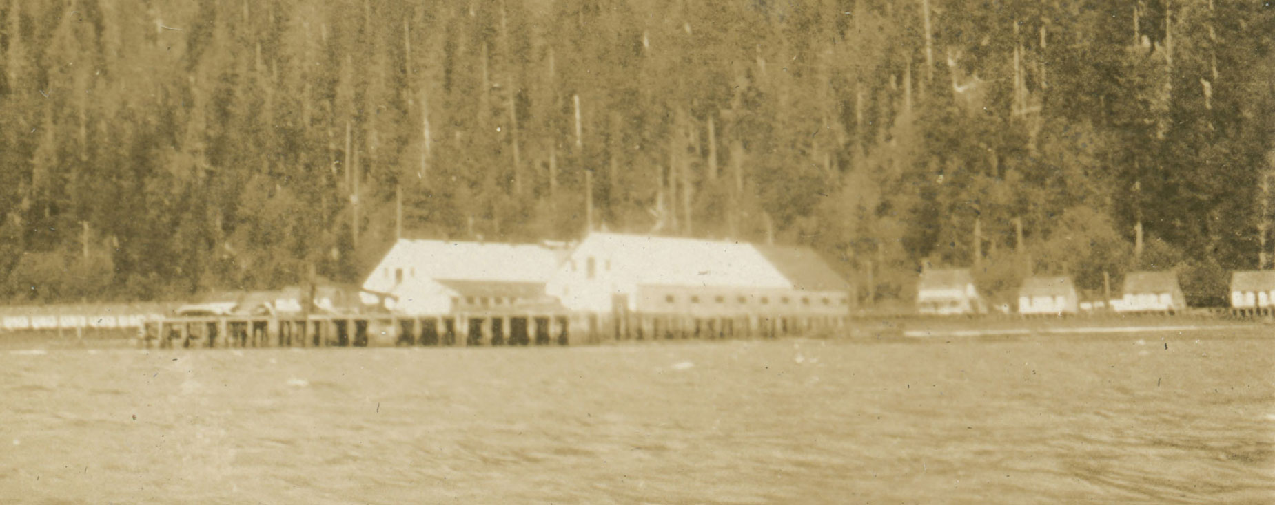 Main cannery building and docks in the distance with the Skeena River in the foreground.