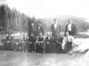 Groupe d'hommes sur un quai; sept assis et quatre debout.